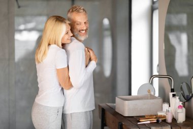 Sevecen son sınıf çifti gündelik banyolarında sevgi dolu bir kucaklaşmayı paylaşıyorlar, mutlu karı koca kucaklaşıyorlar ve evde sabah güzellik rutini yaparken gülümsüyorlar.