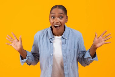 Neşeli siyahi kadın heyecanla omuz omuza bağırıyor, elleriyle sarıya yakın poz veriyor, kamera, stüdyo çekimine bakıyor. Sürpriz ve Olumlu Duygular Konsepti