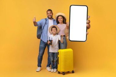 Bavulu ve biletleri olan mutlu siyah aile, beyaz ekranlı büyük boş akıllı telefonu gösteriyor, gülümseyen Afrikalı Amerikalı aileler ve oğulları seyahat rezervasyonları, kolaj ve model için yeni mobil uygulama tanıtıyorlar.