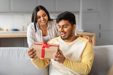 Hoş bir sürpriz. Sevgi dolu Hintli bir kadın kocasına hediye veriyor. Evdeki koltukta oturuyor, gülümsüyor. Mutlu eşine sürpriz yapıyor.