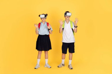 Sırt çantalı iki okul çocuğu sanal gerçeklik kulaklığı takıyor, kollarını kaldırıp savunma pozisyonunda duruyorlar, sarı bir arka plana tamamen dijital bir dünyaya dalmışlar.