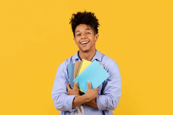 Сияющий Черный Студент Мужчина Обнимает Красочные Блокноты Близко Излучая Удовлетворение — стоковое фото