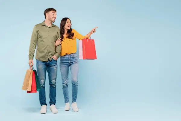 Happy Couple Holding Vibrant Shopping Bags Pointing Something Interesting Side — Stock Photo, Image