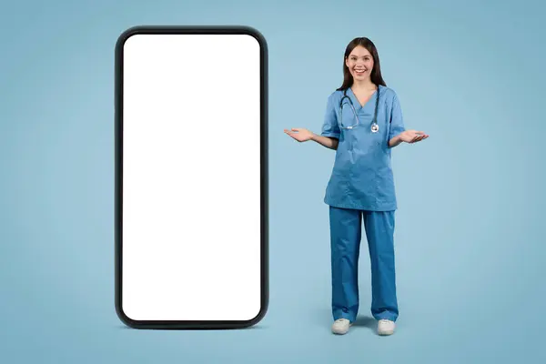 Uśmiechnięta Pielęgniarka Fartuchu Prezentująca Aplikację Mobilną Opieki Zdrowotnej Gigantycznym Modelu — Zdjęcie stockowe