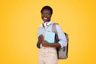 Kitapları olan, sarı arka planda ve stüdyoda izole bir şekilde ders çalışmaktan hoşlanan Afro-Amerikan olumlu genç bayan öğrenci. Eğitim, öğrenim ve okul, üniversite, üniversite