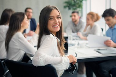 İş arkadaşlarıyla yapılan toplantı sırasında kameraya gülümseyen olumlu sekreter