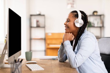 Kulaklıklı gülümseyen siyah bayan bilgisayarına bakıyor, muhtemelen eğlenceli bir e-öğrenme oturumuna katılıyor ya da sanal sınıf, yan görüş, modelleme