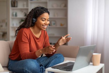 Telekonferans. Kulaklıklı siyahi kadın laptopta video görüşmesi yapıyor, kameraya gülümseyen ve hareket eden Afrikalı Amerikalı kadın, çevrimiçi iletişimin tadını çıkarıyor, boşluğu kopyalıyor.