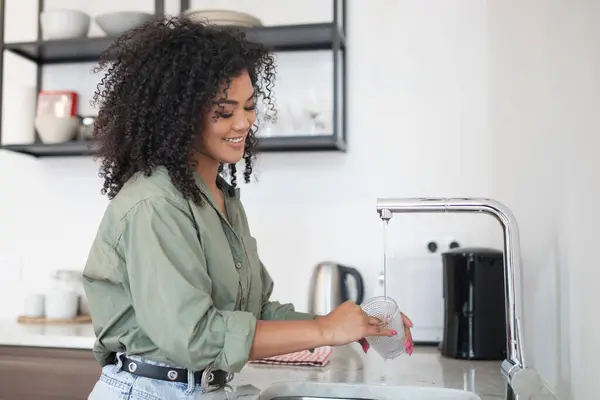 Morning Chores. Happy Brazilian woman stands by the sink washing cup, doing dishes at home kitchen. Lady tackles her daily routine in modern apartment interior. Daily housework