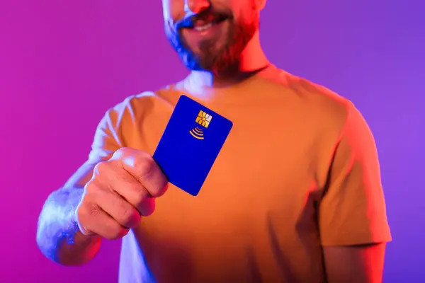 Millennial Man Showcasing Blauwe Plastic Creditcard Tegen Paarse Neon Achtergrond — Stockfoto