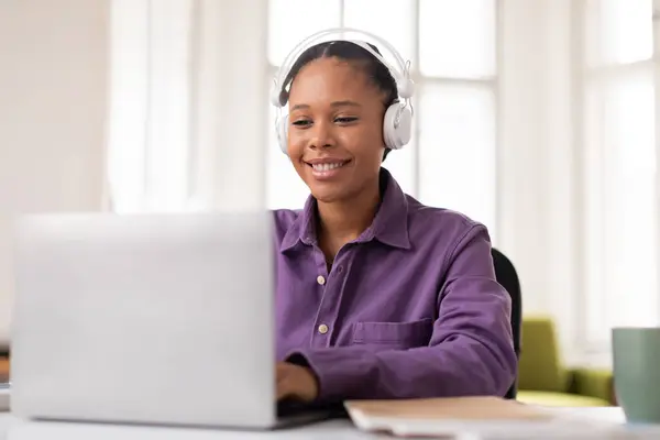 身穿白色耳机的心满意足的非洲裔美国少女把注意力集中在笔记本电脑上的电子学习课程上 旁边有笔记本和咖啡 — 图库照片