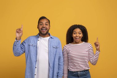 Fikir kavramı. Neşeli Afrikalı Amerikalı çift parmaklarını havaya kaldırıp kameraya bakıyor, heyecanlı siyah eşler ilham verici bir an yaşıyor, problem çözümü buluyor, sarı arka planda poz veriyorlar.