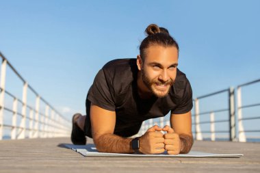 Yaz egzersizleri. Aktif giyimli kararlı sporcu, iskelenin yanında dirsek kalası yaparak çekirdek kuvveti uyguluyor. Sağlıklı erkek yaşam tarzı ve zindelik motivasyonu