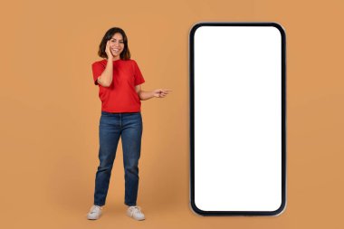 Harika bir online teklif sunan harika genç Arap kadın, beyaz ekranlı büyük bir akıllı telefonu işaret ediyor, renkli arka planda izole edilmiş, reklam için uzay modelini kopyalıyor.