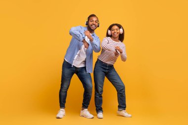 Neşeli genç siyah çift sarı kulaklık takıyor sarı stüdyoda dans ediyor, mutlu Amerikalı erkek ve kadın birlikte eğleniyor, ritimle eğleniyor, kopyalama alanı ile tam uzunlukta.