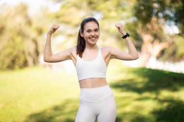 Beyaz spor sutyen ve taytlı mutlu, ince, neşeli, beyaz bir kadın atlet güneşli bir parkta kaslarını esnetiyor. Sağlıklı bir hayat tarzı, mükemmel bir vücudu var.