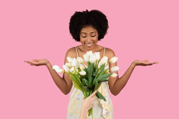 ジョイフル驚いたミレニアムアフリカ系アメリカ人女性 自然なカーリーヘア 穏やかに白いチューリップの花束を保持し ピンクの背景 スタジオでオープンハンドで遊んで提示 — ストック写真