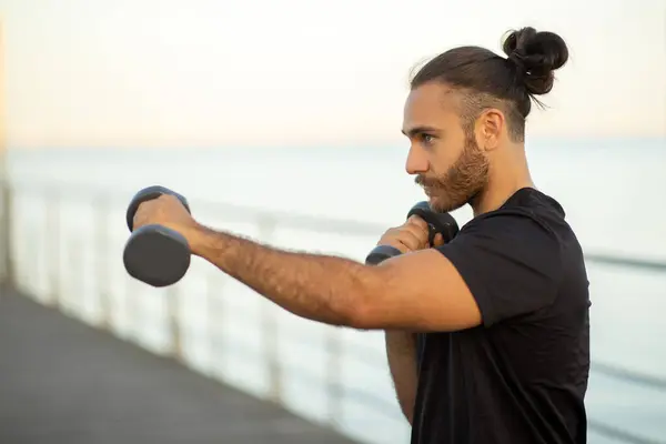 健康在行动 强壮的年轻肌肉男拿着哑铃和拳击 在海堤边展示着决心和力量 在户外运动中精力充沛地锻炼着 从侧面看 — 图库照片