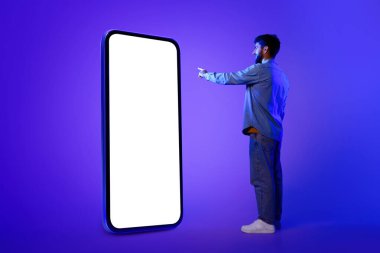 Dijital Boş Zaman. Avrupalı adam büyük bir akıllı telefonun üzerinde duruyor, boş bir ekranı işaret ederek uygulama ya da iletişim konseptleri sunmak için mükemmel, neon mavisi stüdyo arkaplanı