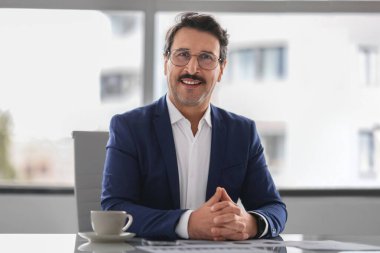 Bıyıklı, mavi takım elbiseli, kendinden emin ve orta yaşlı Avrupalı işadamı bir fincan kahveyle masaya oturmuş, karizma ve profesyonellik yayıyor. İş, iş.