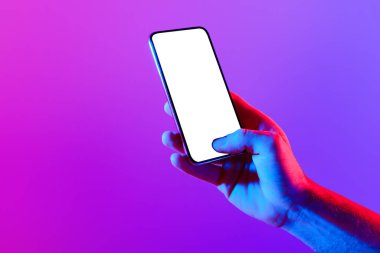 Dijital Bağlantı. Mobil uygulamalar tanıtımı için gösterilen, neon mor arkaplan üzerinde boş ekranlı cep telefonlu genç adamın kırpılmış görüntüsü.