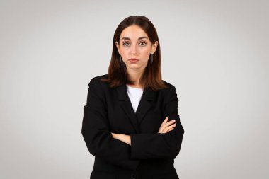 Uzun kahverengi saçlı ve siyah takım elbiseli, kendinden emin beyaz bir iş kadını kollarını çapraz açıp şüphecilik ya da hafif bir hoşnutsuzluk ifadesi sergiliyor.