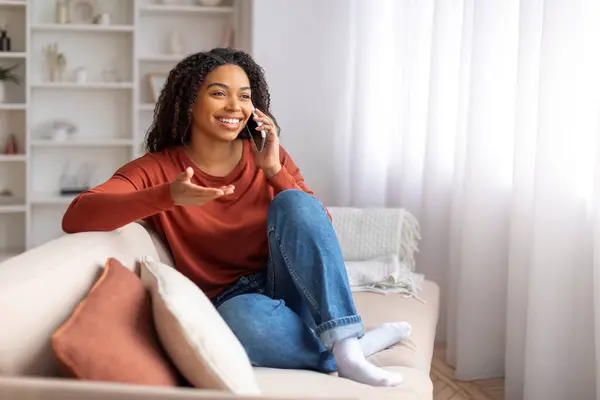 stock image Pleasant Chat. Happy Young Black Woman Smiling While Talking On Cellphone At Home, African American Female Enjoying Mobile Phone Conversation While Relaxing On Couch In Living Room, Copy Space