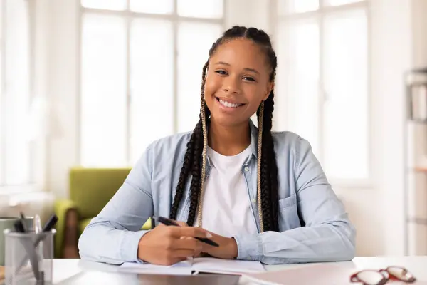 ハッピーブラックレディース学生 手でペンと彼女の机に座ってブレード ノートを書く オンライン教育セッションの準備を示す明るい笑顔 — ストック写真