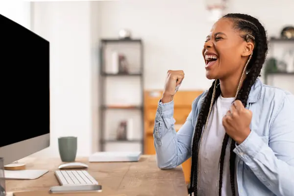 兴奋的拿着耳机的年轻黑人女孩在电脑桌前兴高采烈地举起拳头 庆祝学业上的成功 或在家里学习时获胜 — 图库照片