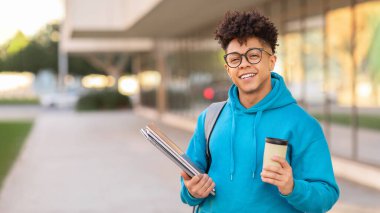 Bilgisayarlı ve kahveli mutlu Afrikalı Amerikalı öğrenci modern üniversite binasında kameraya gülümsüyor. Öğrencilik ve eğitim. Kopyalama alanı olan Panorama