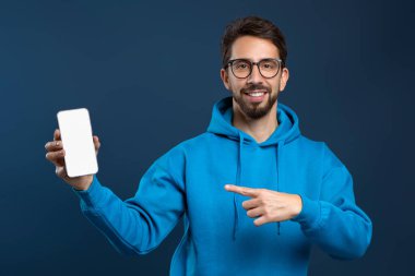 Çevrimiçi reklam. Mavi Stüdyo 'nun arka planında dikilirken elinde boş bir akıllı telefonu işaret eden gülümseyen genç adam, Yeni Uygulama veya Web sitesi, Kolaj, Mockup,
