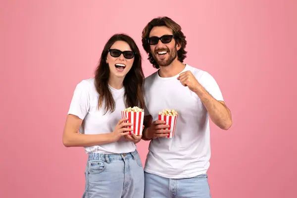 身穿白色T恤衫和太阳镜 头戴红白相间条纹爆米花盒的快乐的白俄罗斯夫妇们 在粉红的背景下享受着欢乐的时光 — 图库照片