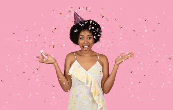 静かなミレニアル世代のアフリカ系アメリカ人女性で パーティーの帽子を被り セッティに囲まれ ピンクの背景に広い笑顔で幸せを表現しています — ストック写真