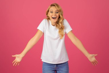 Vay canına. Sarışın, beyaz, neşeli bir kadın. Stüdyoda pembe arka planla duruyor. Kollarını açıp şaşkınlık ve coşkuyla poz veriyor.