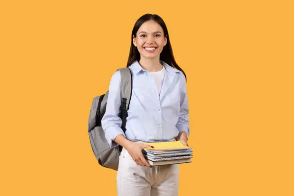 カジュアルな服装の自信を持った女性学生は バックパックとノートブックのスタックを運び 学習の日の準備ができて 黄色の背景にポーズ — ストック写真