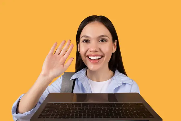 Friendly Female Student Waves Hello Online Class Yellow Backdrop Suggesting — Stock Photo, Image