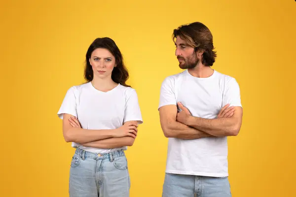 严肃的欧洲青年男女 身穿浅白的T恤衫和蓝色牛仔裤 双手交叉地站在一起 在鲜亮的黄色背景下 表现出一种冷漠的态度 — 图库照片