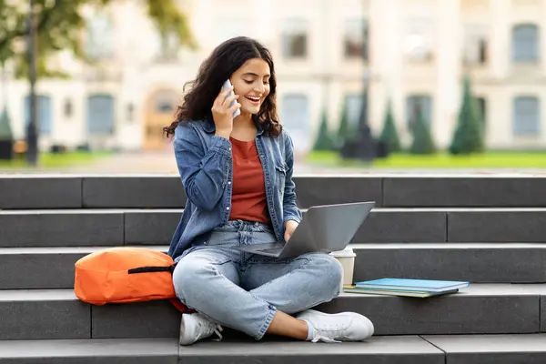 大学のキャンパスで宿題をしている若い東部の女性の学生は 彼女の膝の上にラップトップと階段に座って 携帯電話を使用して 同級生を呼び出し 助けを求め スペースをコピー — ストック写真