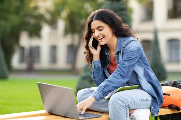アルバイト 学生のためのフリーランス かなり若いインドの女性は コンピュータのラップトップを使用して 雇用主と電話で話し 公共の公園でベンチで冷やし 無料のスペース — ストック写真