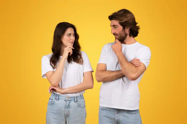 一对穿着白色T恤衫和牛仔裤的心事重重的欧洲年轻夫妇 面面相觑 带着沉思的表情 暗示着在黄色背景下进行深入的对话或决策 — 图库照片