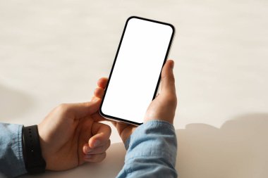 Mavi kot gömlek ve siyah akıllı kaset giyen, akıllı telefonu elinde tutan birinin elleri, teknoloji kullanımını veya mobil iletişimi öneriyor, kırpılmış, kapatılmış