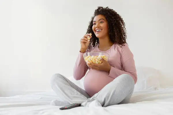 Radosna Ciężarna Czarna Kobieta Jedząca Popcorn Siedząc Domu Łóżku Uśmiechnięta — Zdjęcie stockowe