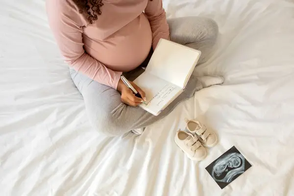 Těhotná Žena Doma Zapisuje Myšlenky Sešitu Sedí Posteli Obklopená Malými — Stock fotografie