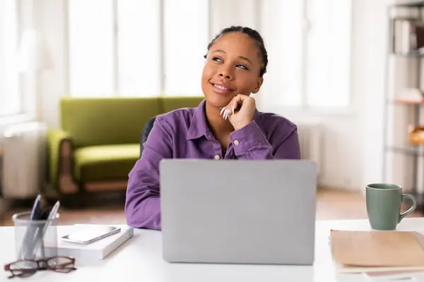 紫色のシャツデイで思慮深い女性学生は 彼女のラップトップでオンラインで勉強しながら 脇を見 コーヒーを蒸し 彼女の側で教材を勉強しながら — ストック写真
