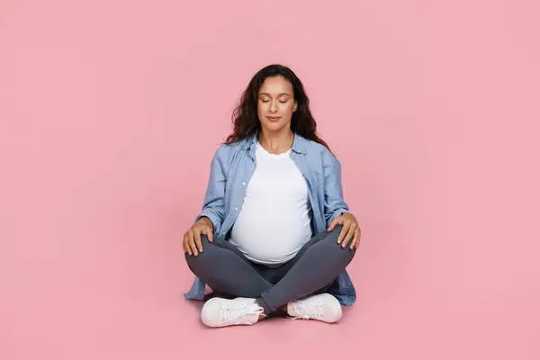 平和な若い妊娠中の女性は 閉じた目で床に座り ピンクのスタジオの背景に隔離された瞑想をしています ストレス軽減 妊娠中のヨガの練習 — ストック写真
