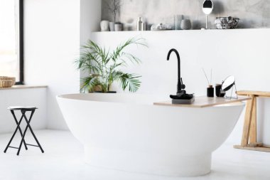 Şık, minimalist banyo, modern serbest stil küveti, siyah armatürleri ve doğal ışıklandırmayla aydınlatılmış doğal dekor unsurlarıyla şık bir odanın iç çekimi, kopyalama alanı.