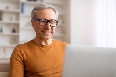 Evde bilgisayar ekranına bakıp gülümseyen, gözlüklü, neşeli, gri saçlı, gözlüklü yaşlı adamın yakın çekimi. Büyükbaba internetten uzak bir iş arıyor, boşluğu kopyala