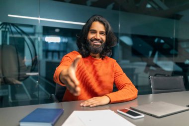 Gülümseyen dost canlısı, sakallı, milenyum Hintli adam yöneticisi modern ofisin masasında oturuyor, kameraya elini uzatıyor, iş ortağı ya da çalışanı karşılıyor, iş görüşmesi yapıyor.
