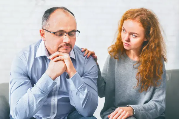 Supportive wife comforting her upset husband at meeting in counselors office, encouraging him to share problems