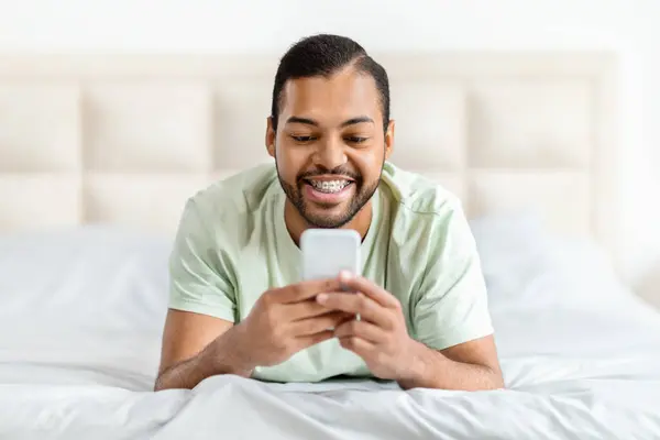 Крупный План Счастливого Красивого Африканского Американца Пижаме Использующего Телефон Лежит — стоковое фото